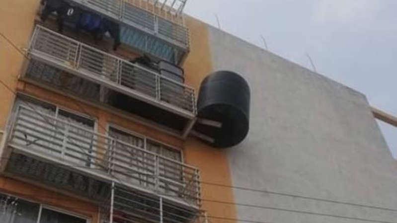 Tinaco 'cuelga' de dos trozos de madera afuera de un edificio; temen tragedia